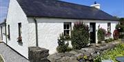 Dunnaglea Cottage taken from the front left. The one-storey cottage has a half-leaf front door, and has flowers outside.