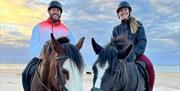 a man and woman sitting on horse back on the beach