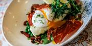 a salad dish with poached eggs and proscuitto