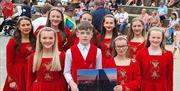 Irish dancers in costumes hold a sign saying 'Red Sails Festival Portstewart'