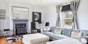 Elegant guest lounge at Willow House featuring a large light blue sectional sofa, decorative fireplace, white chandelier, and black-and-white striped
