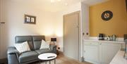 The Wishing Chair sitting area with yellow feature wall, with grey leather sofa, two-tone circular white and black coffee table and a wooden armchair.