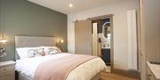 The Basalt bedroom with a green feature wall, with double bed and upholstered headboard, centred between 2 bedside lockers with natural light from the