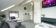 The Fisherman’s Reel sitting area with sloping ceiling and dormer window, neutral décor, green/grey carpet and grey leather settee and wall-mounted Sm
