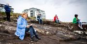 Participants of the workshop sit with sketch pads on coastal rocks in Portrush