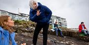 Frankie Creith talks to a workshop participant who is sitting on coastal rocks in Portrush