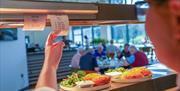 a chef looks at a ticket above a serving station in a restaurant that holds plates of food