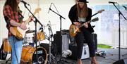 A band on stage with two male guitar players, a  man drumming and a female singer with a guitar