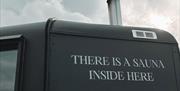 Side of matte black sauna with writing reading "there is a sauna inside here"