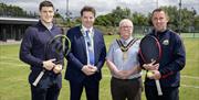 four men stand for a photo on a tennis court, 2 are holding rackets