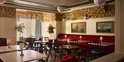 interior of Red Sails dining area at Portrush Adelphi which features red upholstered seating and chairs, with small lamps on every table.