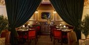 interior of the Red Sail Room dining area at Portrush Adelphi. Large velvet curtains drape either side of a snug alcove where there are various dining