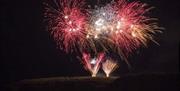 Fireworks burst to life above the sea and rocks