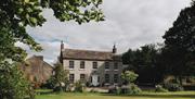 A traditional country house, the picture is taken from across a beautifully kept garden with well kept bushes and small trees.
