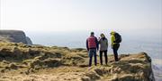 three people are standing close to a cliff edge looking at the view