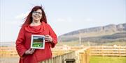 a woman holding a framed piece of felting artwork, with the cliffs of Binevenagh in the background