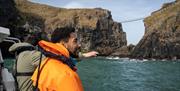 Group on a boat enjoying the Giant Shipwrecks of the North Coast experience with Carrick-A-Rede Rope Bridge in the background