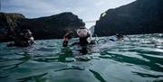 Group in wetsuits in the water with Carrick-a-Rede Rope Bridge in the background as part of a scuba diving experience with Aquaholics