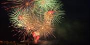 Fireworks burst to life above the sea and rocks, with the college in the background