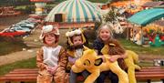 Three smiling children sitting on a bench, with two in animal costumes.