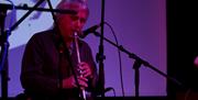 a man plays a tin whistle on stage with a microphone infront of him