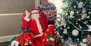 Santa sits beside a large Christmas tree at The Causeway Hotel, surrounded by Christmas sacks