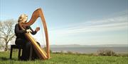 lucia mcginnis plays the irish harp outside with Lough Foyle in the background