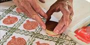 a person's hands using a stamp in the shape of a pomegranate to create printed patterns on linen