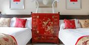 Elegant B&B bedroom with two double beds, red embroidered runners, accent pillows, and an ornate red oriental chest between the beds.