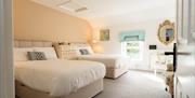 Spacious B&B suite featuring two double beds with white linens, neutral walls, carpeted flooring, and a decorative gold framed mirror.