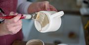 A person's hands are painting the bottom of a ceramic mug