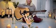 Amanda St John pictured with guitar surrounded by candles and floral arrangements