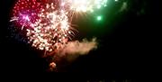 Fireworks burst to life above the sea and rocks