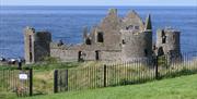 The photo is of Dunluce Caste. The Castle is old and run down.  The sea is in the background. A green field is in the foreground.