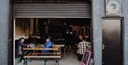 a roller door is opened to reveal people sitting inside at picnic benches at Lacada Brewery