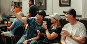 a group of people take a selfie while sitting in a communal area at Lacada Brewery. They are holding beer glasses.