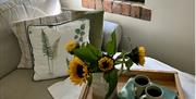 a wooden tray with two mugs and a vase of sunflowers sits on a sofa with green cushions at Wrens Nest
