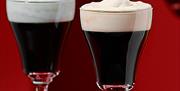2 Irish coffees side by side, with creamy heads on a red background.