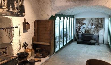 inside view of exhibits in museum looking down a passageway with some items attached to wall, some on floor, and a glass fronted display case on left.