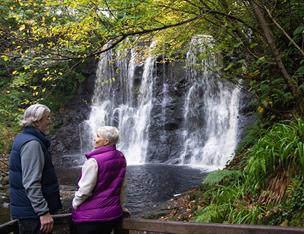 two people stand taking in the views of a secluded waterfall at Glenariff Forest Park