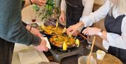 cookery class students work around a table making freshly cooked paella