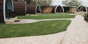 Five glamping pods on grass with a paved path