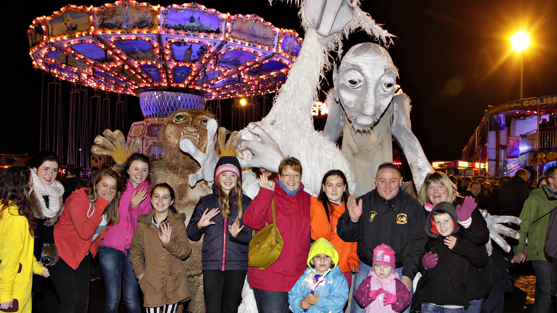 Image shows a group of people standing in front of scary Halloween characters, with a Fairground in the background