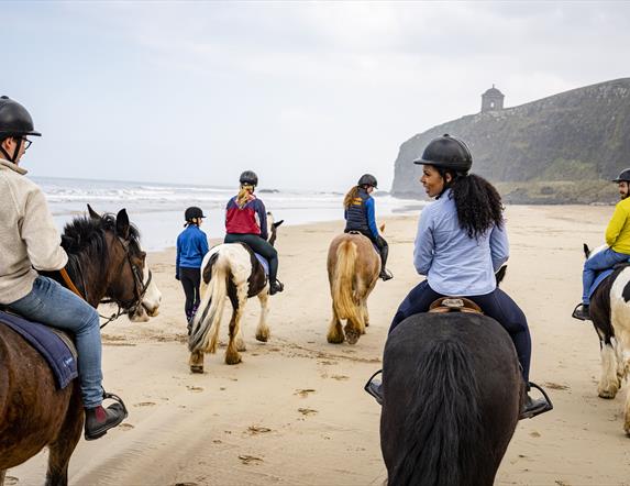 People riding horseback on the beach with Mussenden Temple in the background