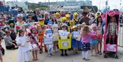 Image shows crowd of children all dressed in fancy dress costumes.  There are children dressed as minions, a barbie doll,  lego characters the tooth f