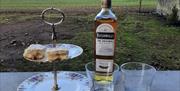 A bottle of Bushmills Whiskey with two glasses. There is a cake stand with baked goods placed on it.