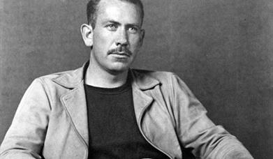Black and white photo of John Steinbeck sitting on a chair 