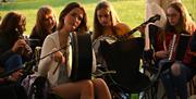 a group of girls playing traditional irish musical instruments including the bodhran, accordian, a banjo and flute