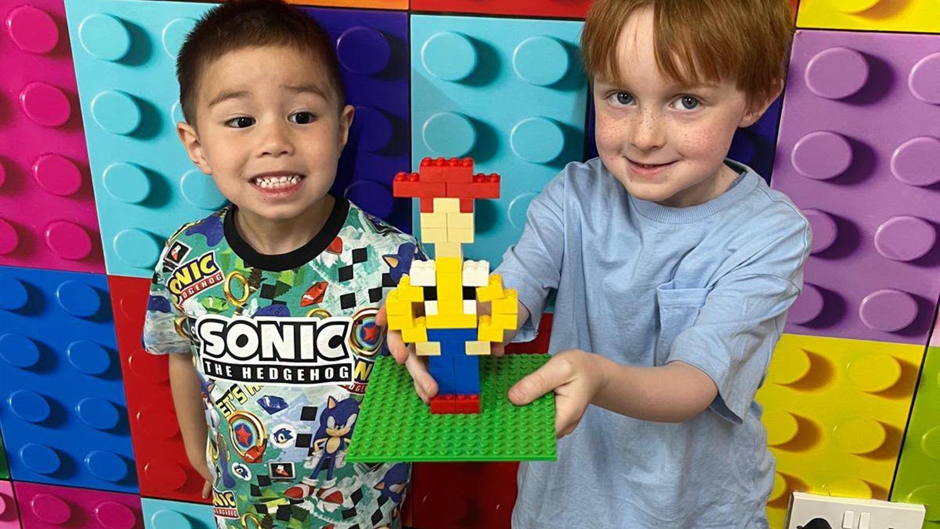 two children holding up a cowboy made of bricks two children holding up a cowboy made of bricks