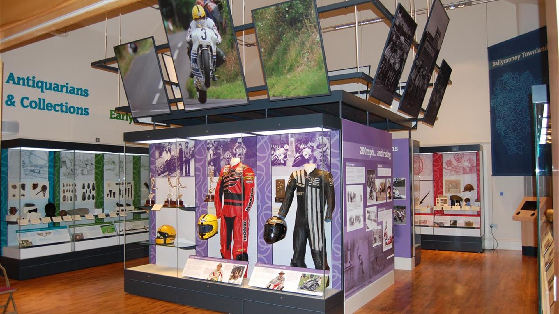 A glazed exhibition space showing racing gear worn by the face road motorbike racer Joey Dunlop